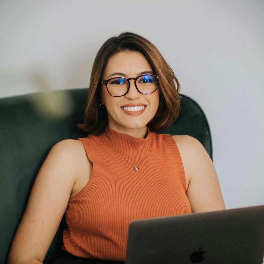 Ana Flávia Vianna, planejadora financeira, sorrindo em uma poltrona verde com o notebook